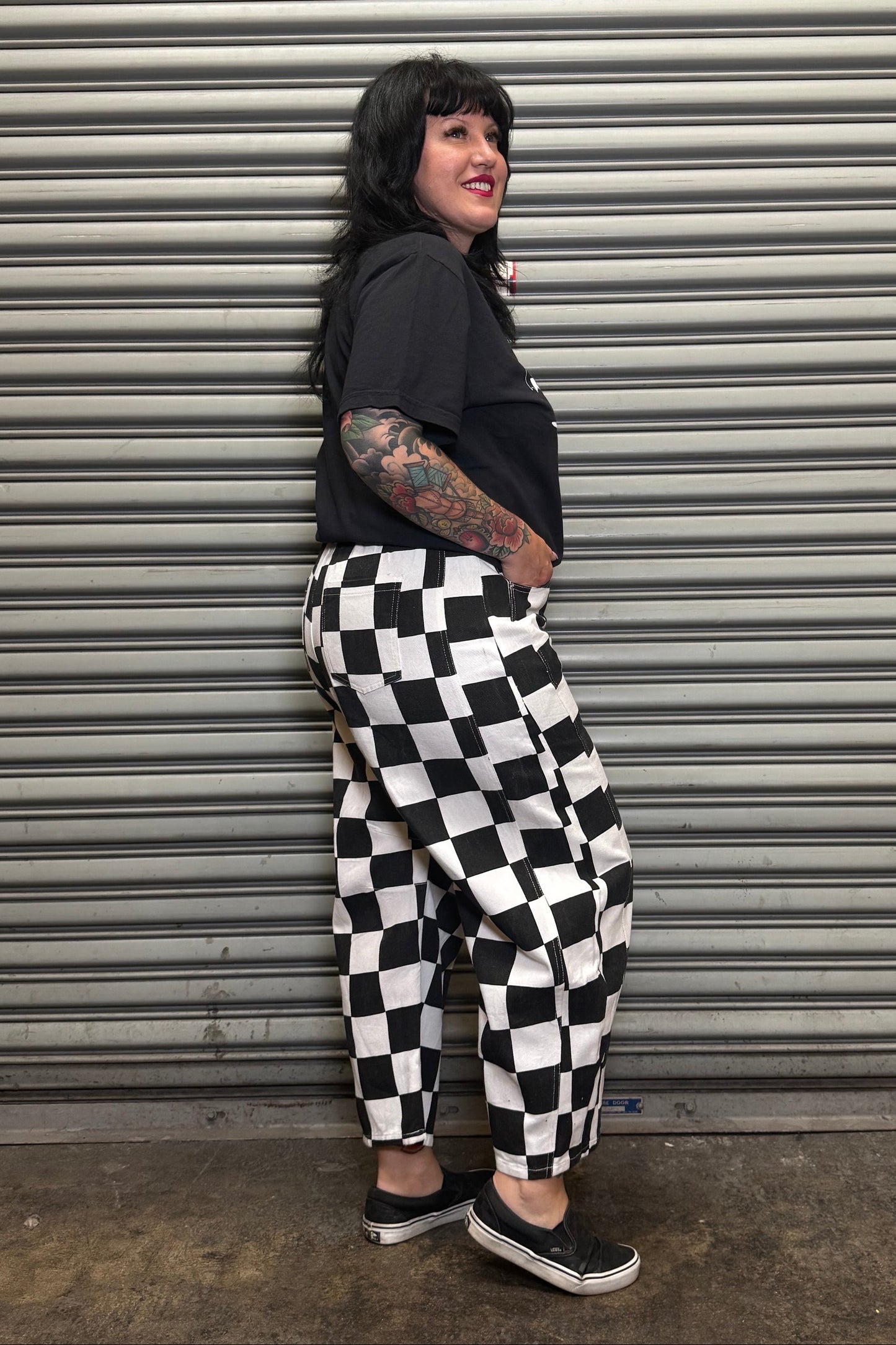 Person wearing a black and white checkered outfit standing in front of a metal shutter.