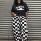 Person wearing a black t-shirt with white graphics and checkered pants standing in front of a metal shutter.