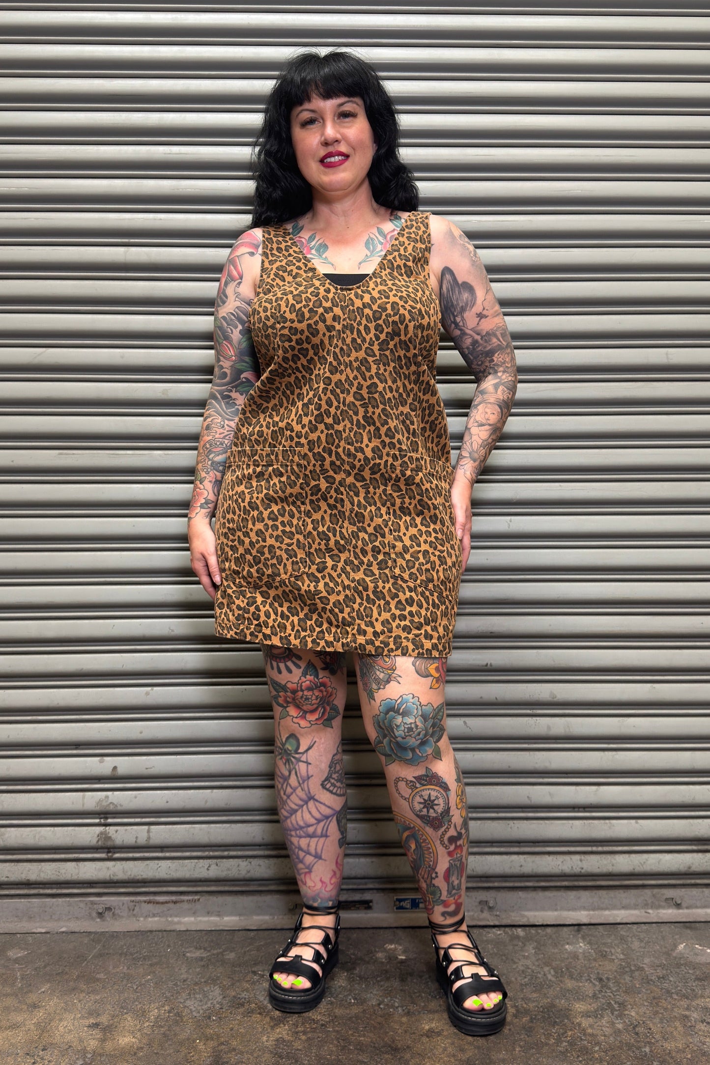 Person wearing a leopard print dress standing in front of a metal shutter.