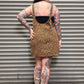 Person wearing a leopard print dress with tattoos standing against a metal shutter.