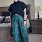 Woman wearing a black top and green leopard print pants in a bedroom setting.