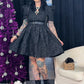 Person wearing a black dress with tattoos standing next to a purple Christmas tree and gift boxes.