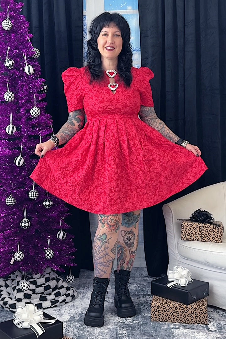 Woman in a red dress posing in front of a purple Christmas tree with decorations.