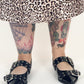 Person wearing black studded shoes with a leopard print skirt and tattoos on a white background