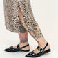 Person wearing leopard print skirt and black sandals with floral tattoos on a white background