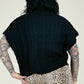 Woman wearing a black cable knit vest over a leopard print skirt on a plain background