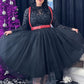 Woman in a black tulle skirt with red harness standing next to a decorated Christmas tree.