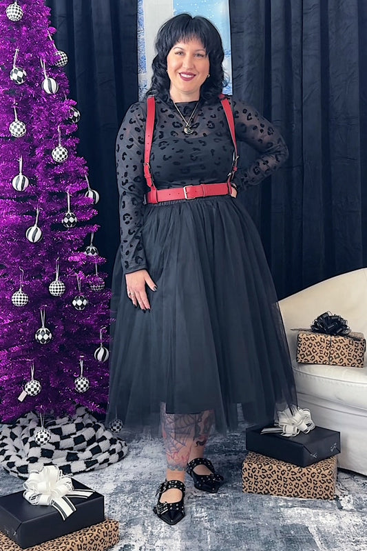 Woman in a black tulle skirt with red harness standing next to a purple Christmas tree.
