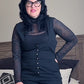 Person wearing a black outfit with sheer sleeves in a bedroom setting