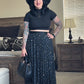 Woman in a black hat and black top with a star-patterned skirt standing in a bedroom.