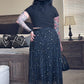 Person wearing a black outfit with a hat in a room with furniture and decor.