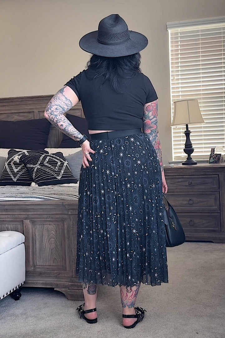 Person wearing a black outfit with a hat in a room with furniture and decor.