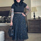 Woman in a black outfit with a hat, skirt, and top standing in a room.
