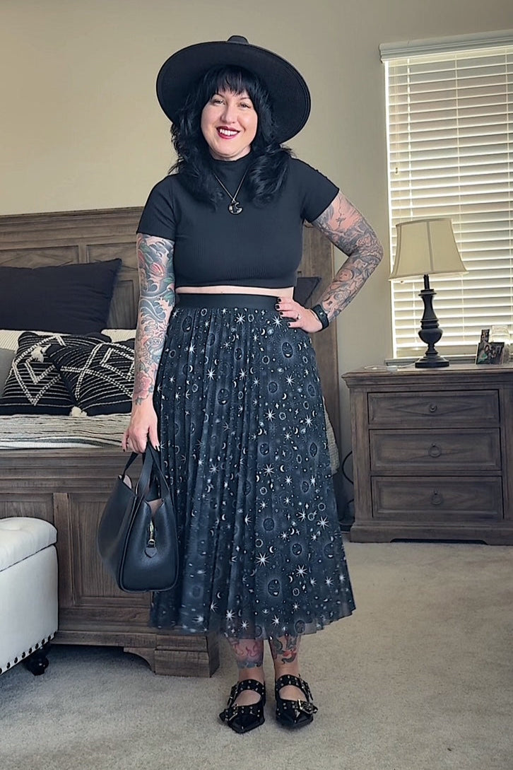 Woman in a black outfit with a hat, skirt, and top standing in a room.
