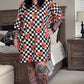 Person wearing a black and white checkered dress with orange pumpkin patterns in a bedroom.