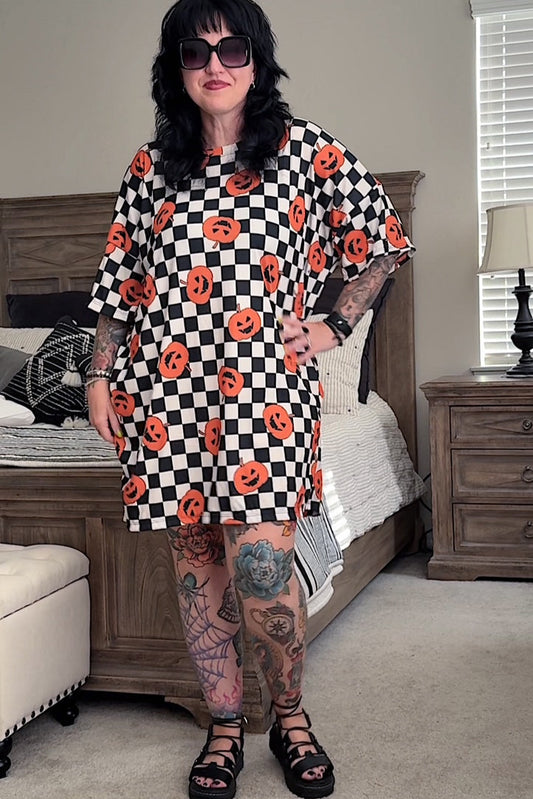 Person wearing a black and white checkered dress with orange pumpkin patterns in a bedroom.