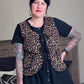 Person wearing a leopard print vest over a black outfit in a living room.