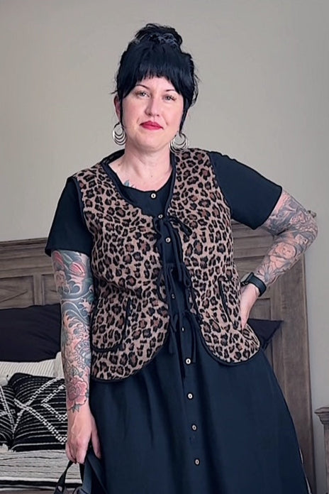 Person wearing a leopard print vest over a black outfit in a living room.