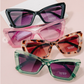 Four pairs of sunglasses with different frame designs and colors on a light pink background.