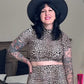 A woman wearing a leopard print pencil skirt with a seamless waistband, paired with a long-sleeve top, black hat, and carrying a black bag.