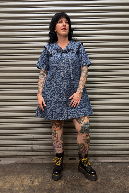 Person wearing a blue denim dress standing in front of a metal shutter.