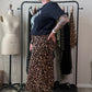 A person modeling a leopard print midi skirt with a black graphic t-shirt and black combat boots, standing in a room with a clothing rack and a dress form.