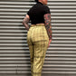 A person lying on their side in front of a gray metal roll-up door, wearing a black short-sleeve top and beige plaid pants with black shoes.