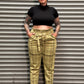 A person wearing a black cropped short-sleeve top and olive green plaid trousers, standing against a gray metal shutter door.