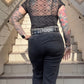 Person with tattoos wearing a sheer top and dark jeans on a staircase.