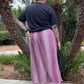 Person wearing a black shirt and pink skirt standing in front of palm trees.