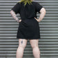 Person wearing a black t-shirt with tattoos visible on arms and legs, standing in front of a metallic shutter.