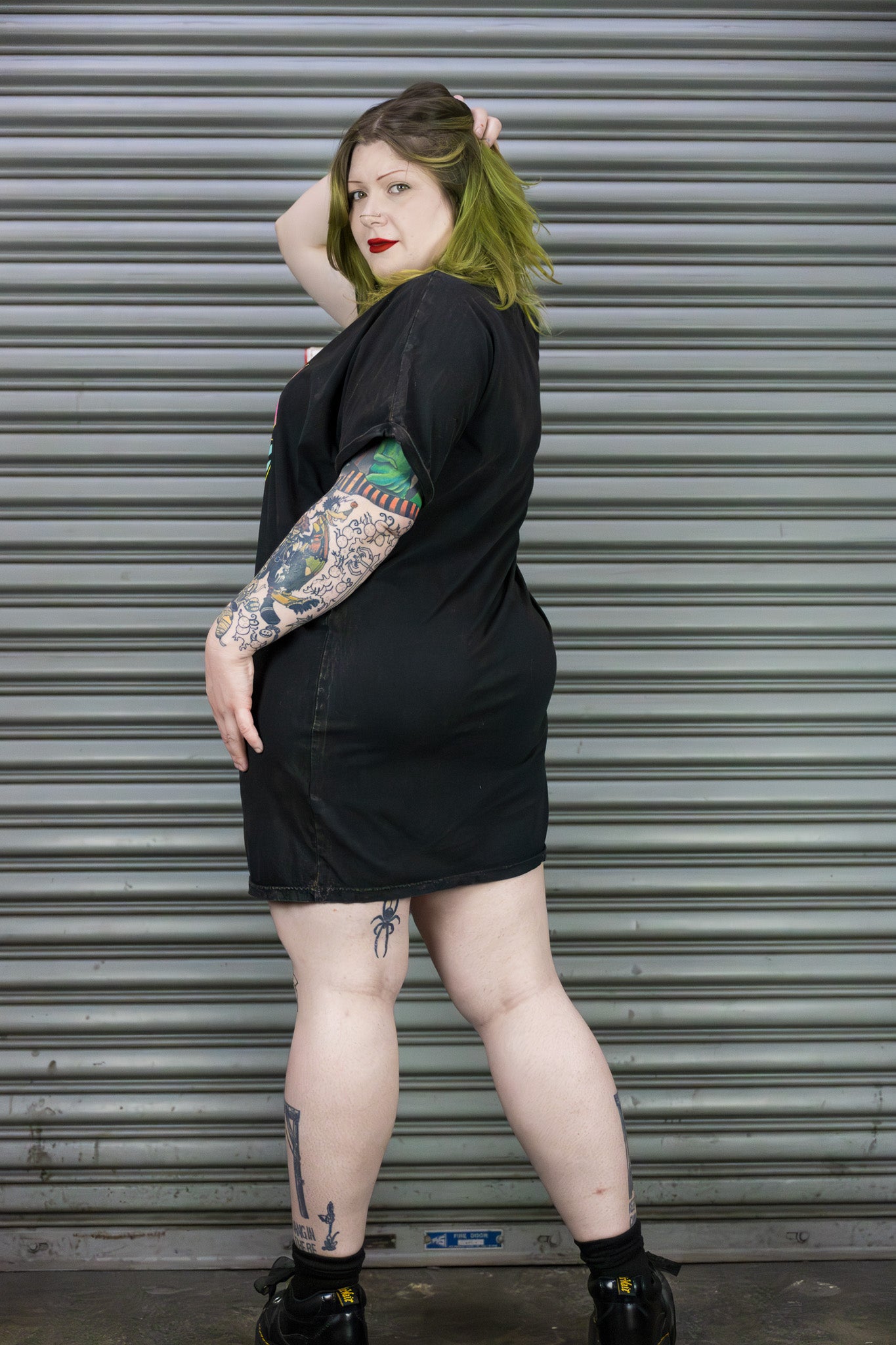 Person wearing a black t-shirt with tattoos standing in front of a metal shutter.