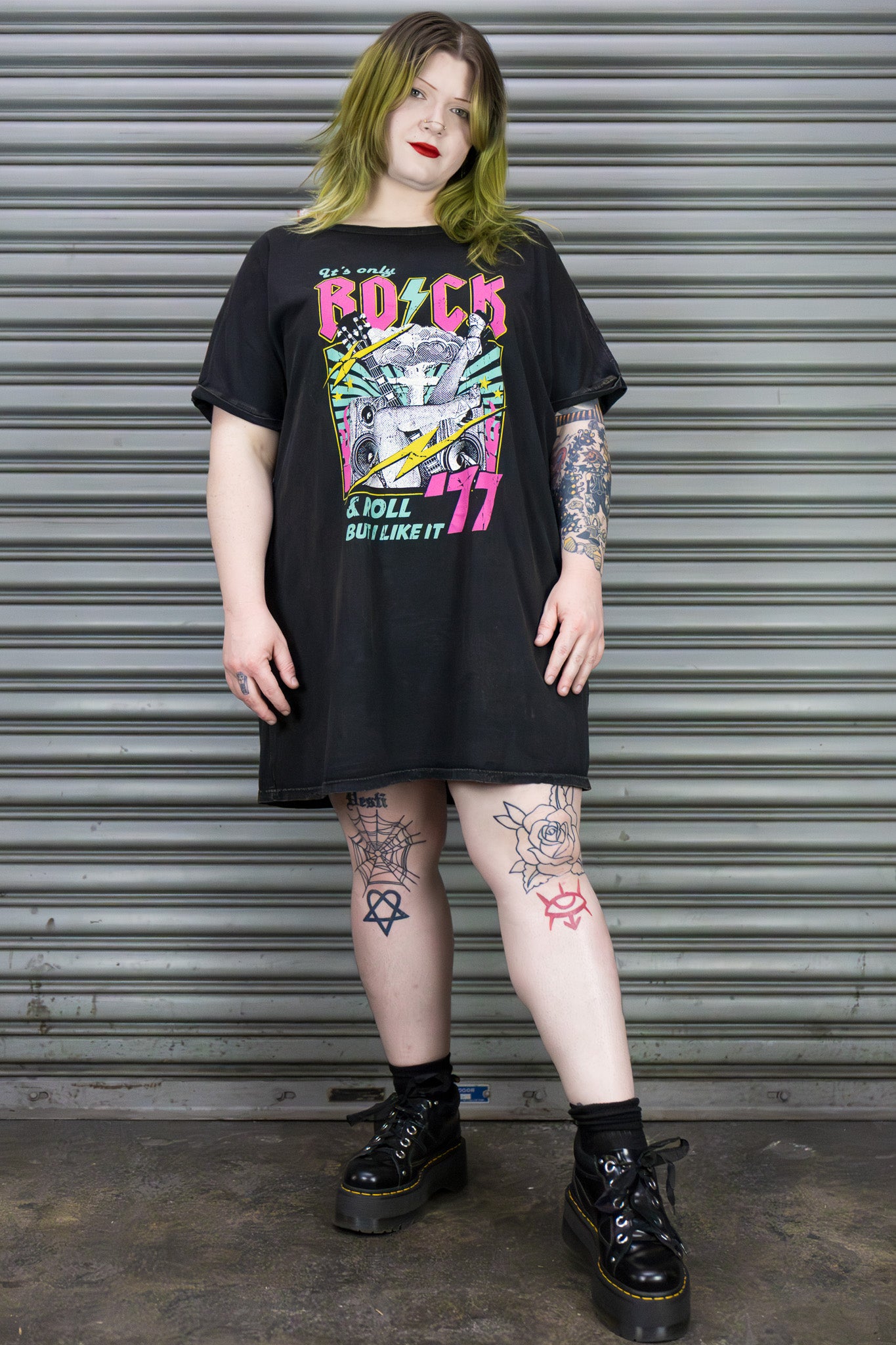 Person wearing a black graphic t-shirt and black boots in front of a metal shutter.