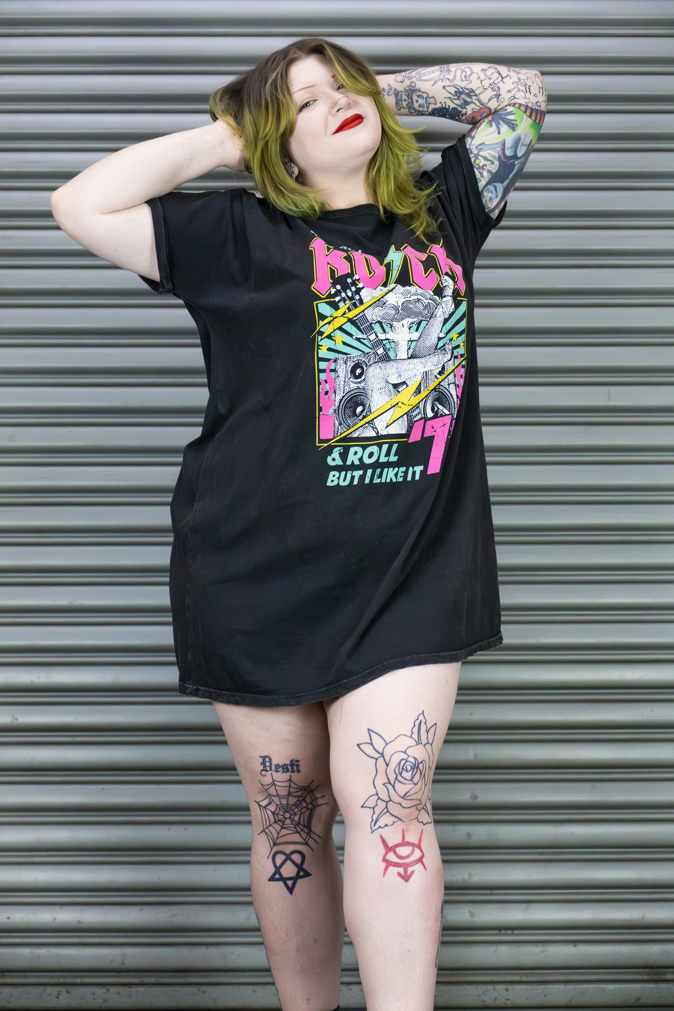 Person wearing a black t-shirt with colorful graphic design in front of a metallic shutter.