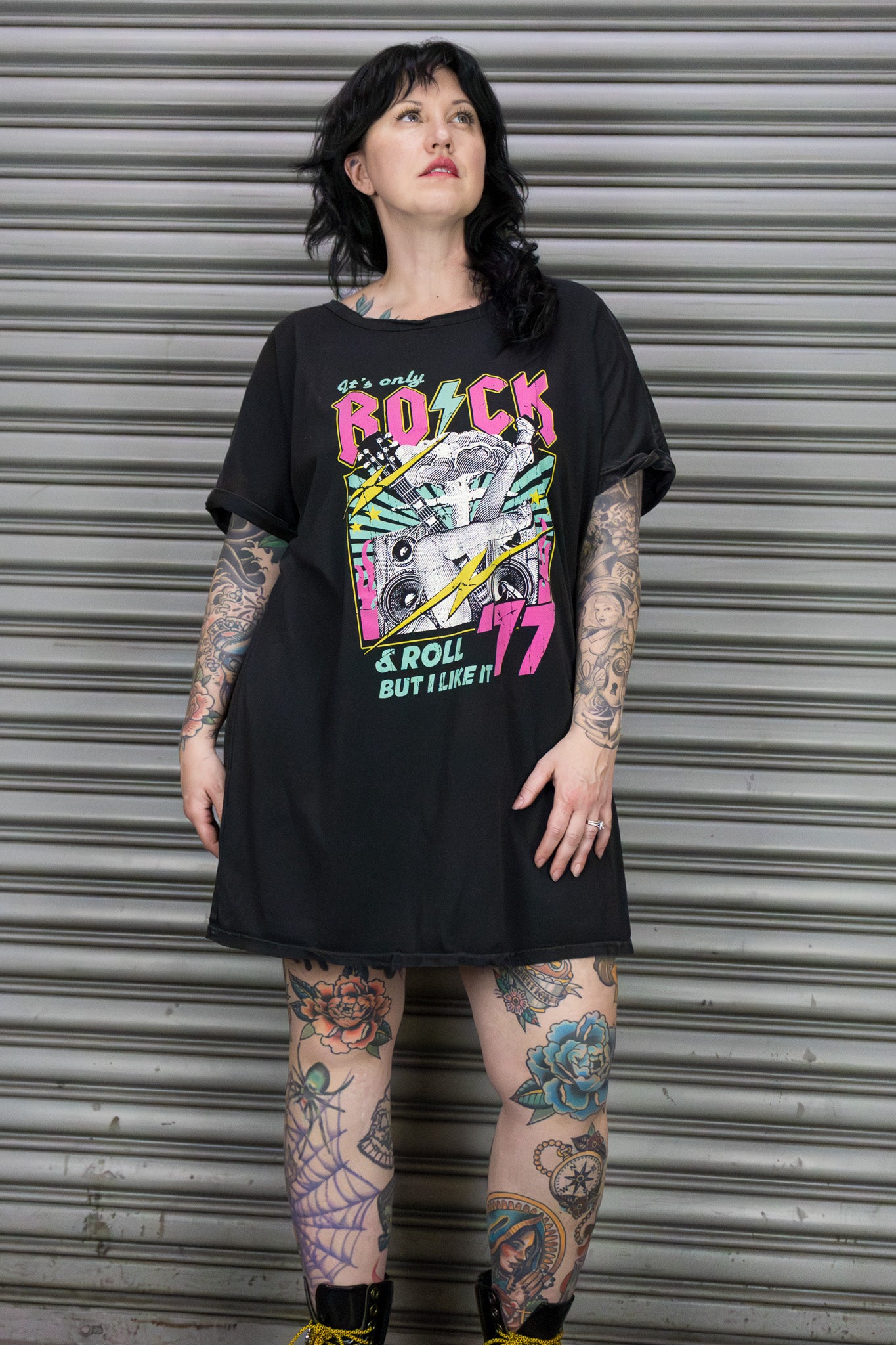 Person wearing a black t-shirt with colorful graphic design in front of a metal shutter.