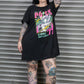 Person wearing a black oversized t-shirt with colorful graphics and text, standing in front of a metal shutter.