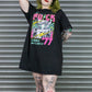 Person wearing a black t-shirt with colorful graphic design in front of a metal shutter.