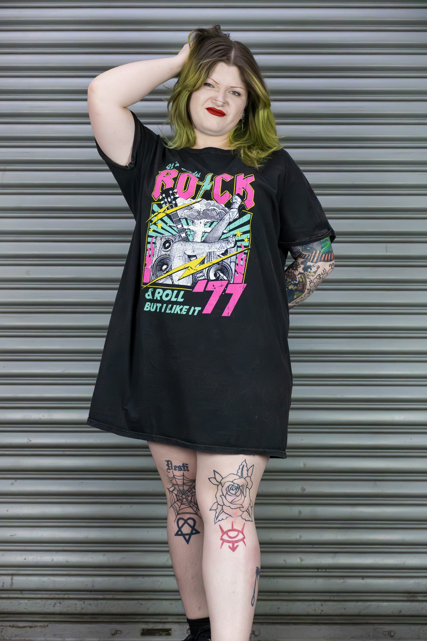 Person wearing a black t-shirt with colorful graphic design in front of a metal shutter.