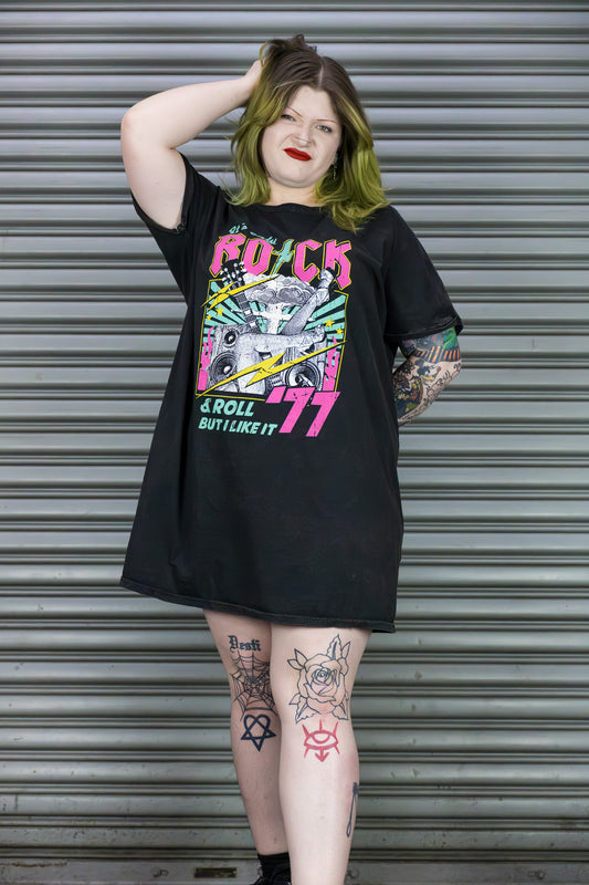 Person wearing a black t-shirt with colorful graphic design in front of a metal shutter.