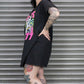 Person wearing a black oversized t-shirt with colorful graphics and shorts, standing against a metallic shutter.