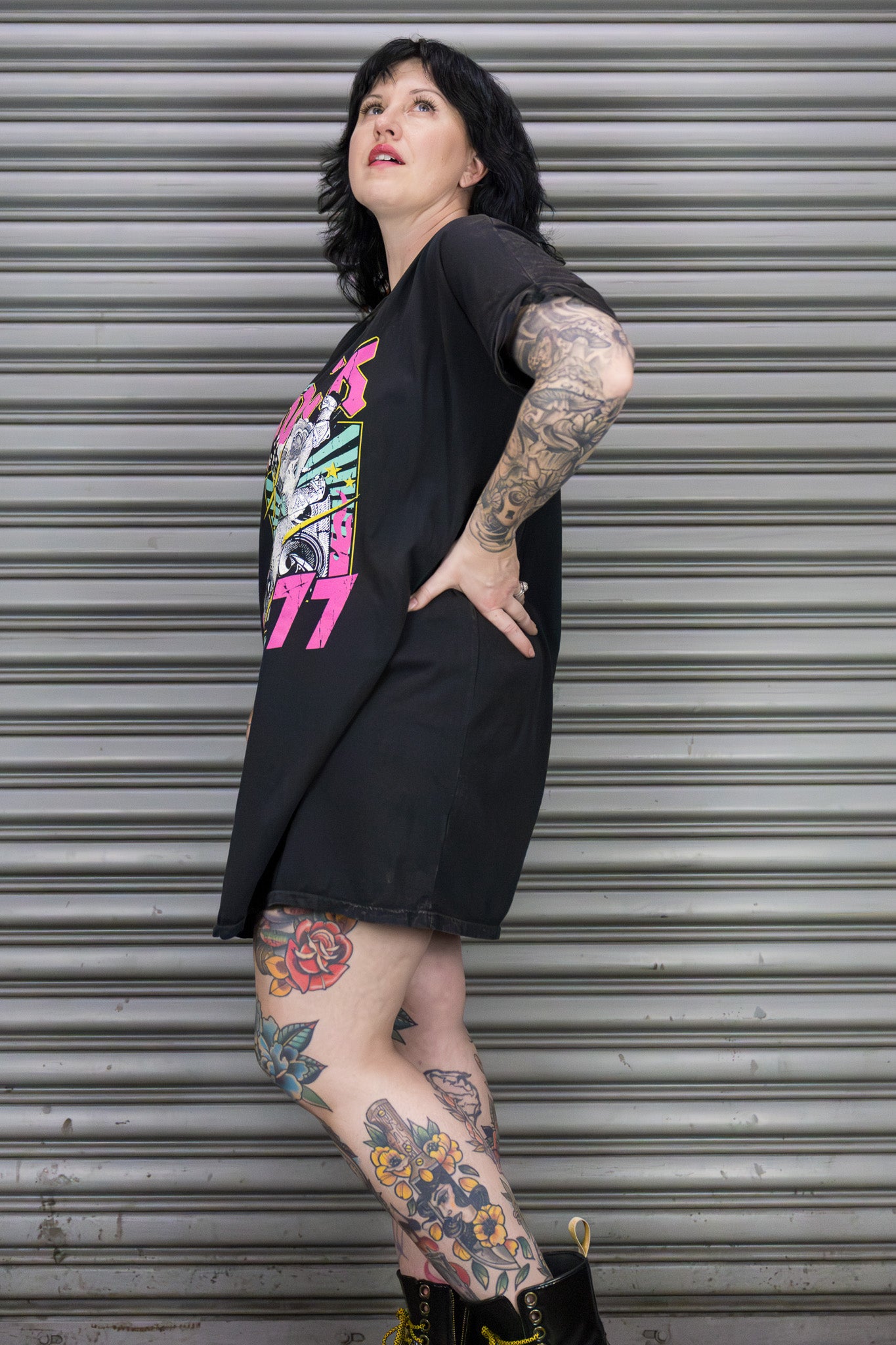 Person wearing a black oversized t-shirt with colorful graphics and shorts, standing against a metallic shutter.