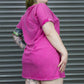 Person wearing a pink dress standing in front of a gray metal shutter.