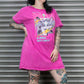 Person wearing a pink t-shirt with a graphic design in front of a metal shutter.