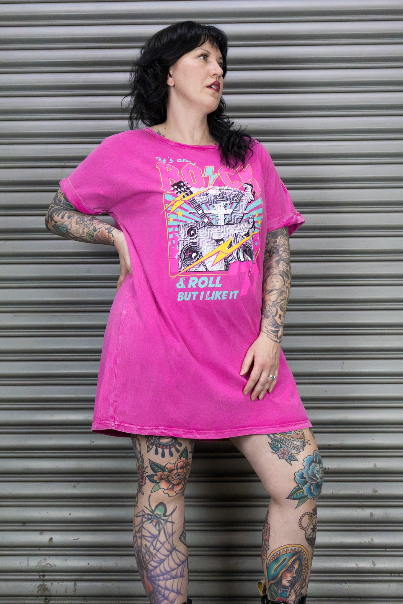 Person wearing a pink t-shirt with a graphic design in front of a metal shutter.