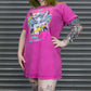 Person wearing a bright pink t-shirt with graphic design in front of a metallic shutter.