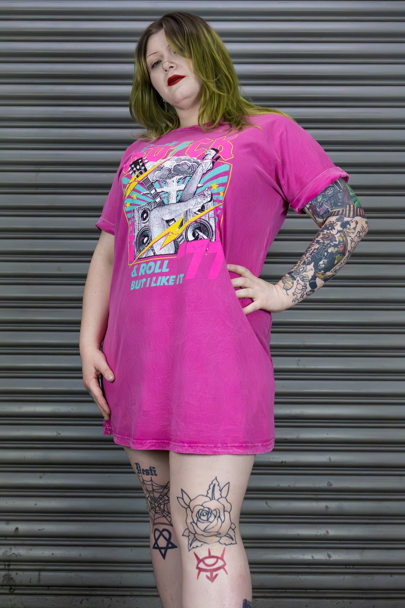 Person wearing a bright pink t-shirt with graphic design in front of a metallic shutter.