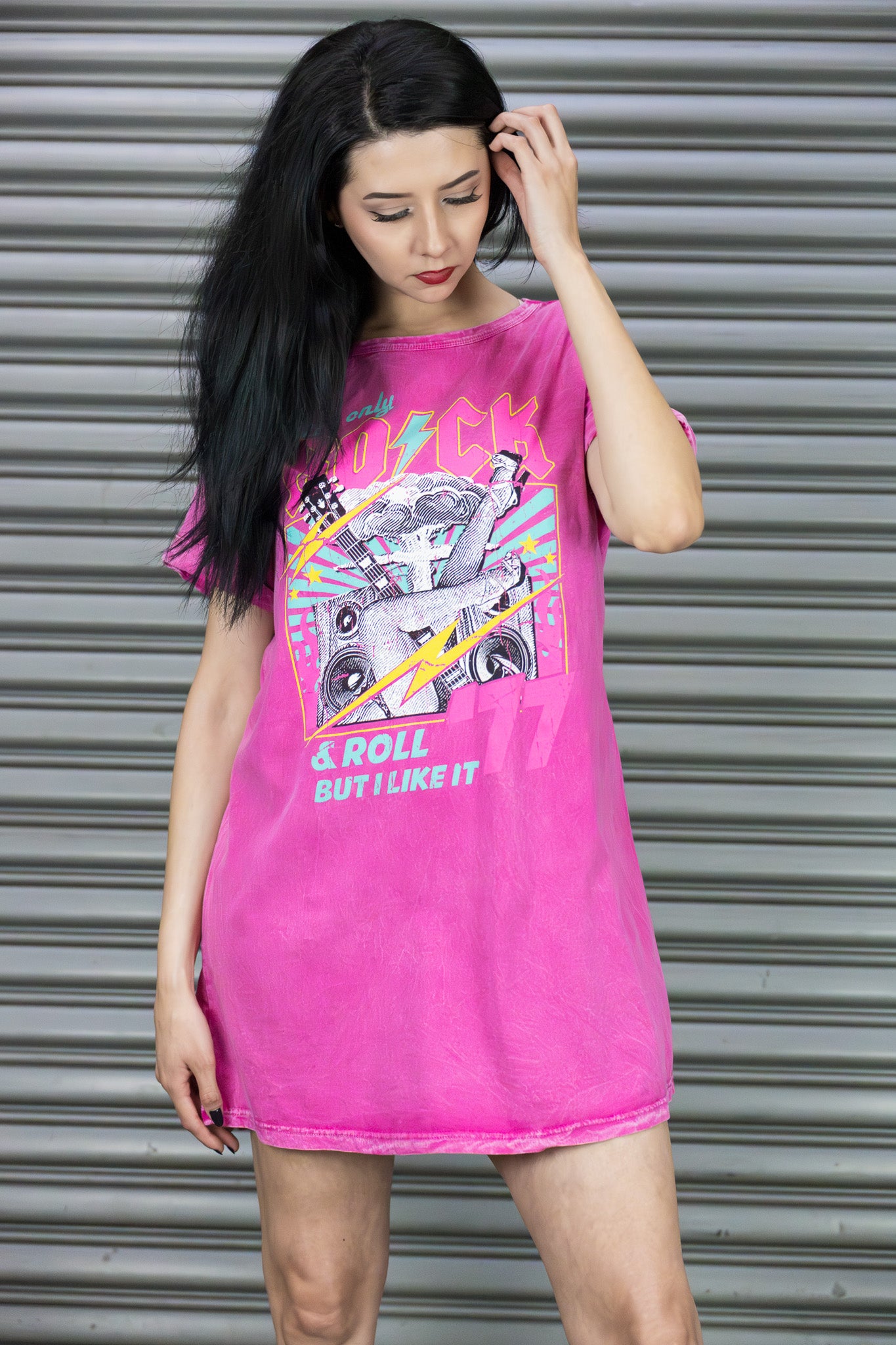 Woman wearing a bright pink t-shirt with graphic design against a metallic shutter background