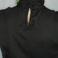 Close-up back view of a black dress on a person, showing a gathered high neck with a keyhole cutout and green hair visible at the top against a light gray background.