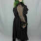 A model wearing a black sheer long-sleeve midi dress with a ruffled collar, paired with black platform boots, standing against a light gray fabric backdrop.