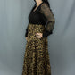 A woman modeling a leopard-print maxi skirt paired with a black long-sleeve top, standing against a gray studio backdrop.